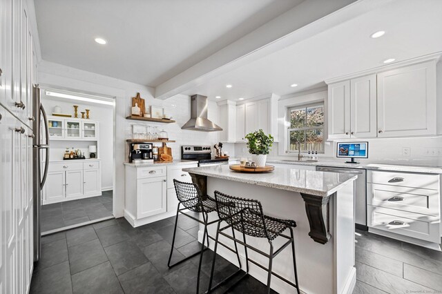 kitchen with sink, white cabinets, wall chimney range hood, and a center island