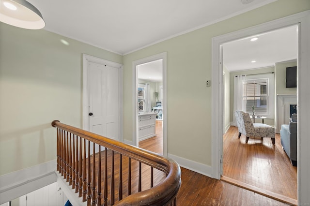 hallway featuring hardwood / wood-style floors, an upstairs landing, baseboards, and crown molding