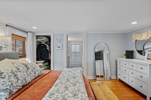 bedroom with ornamental molding, light wood-type flooring, a closet, and a spacious closet