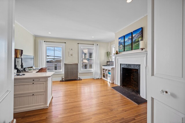 living room featuring a high end fireplace, light wood-type flooring, ornamental molding, and radiator heating unit