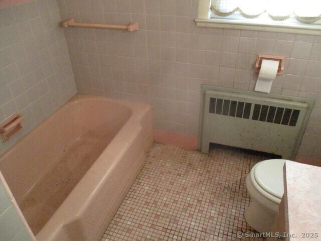 bathroom with toilet, tile patterned floors, tile walls, a bathtub, and radiator heating unit