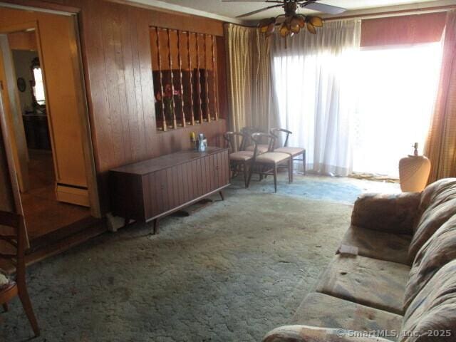 living room featuring baseboard heating, ceiling fan, carpet flooring, and wooden walls