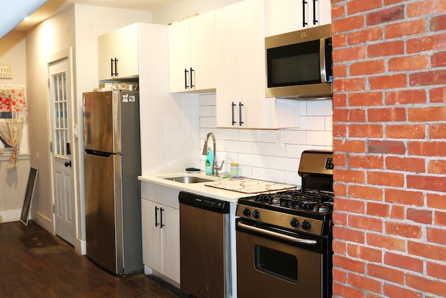 kitchen featuring white cabinetry, sink, dark wood-type flooring, stainless steel appliances, and brick wall