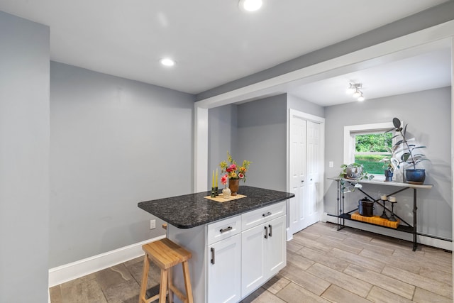 kitchen with a baseboard heating unit, a kitchen breakfast bar, dark stone countertops, light wood-type flooring, and white cabinetry