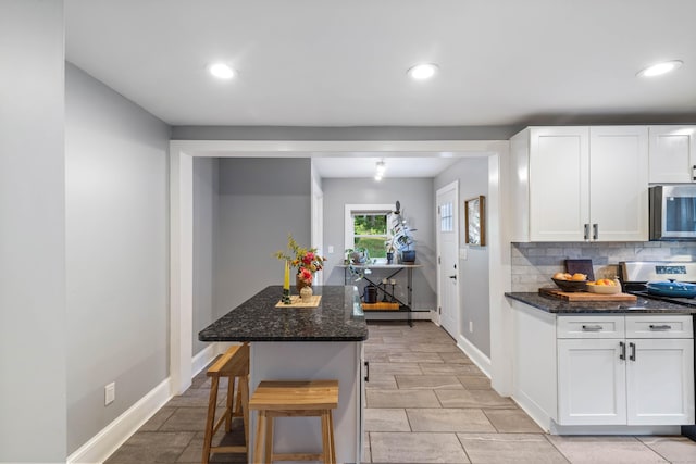 kitchen featuring a breakfast bar area, white cabinets, dark stone counters, and range