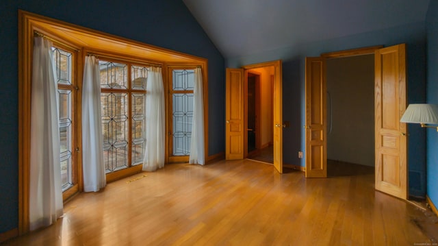 unfurnished bedroom featuring multiple windows, lofted ceiling, and light wood-type flooring