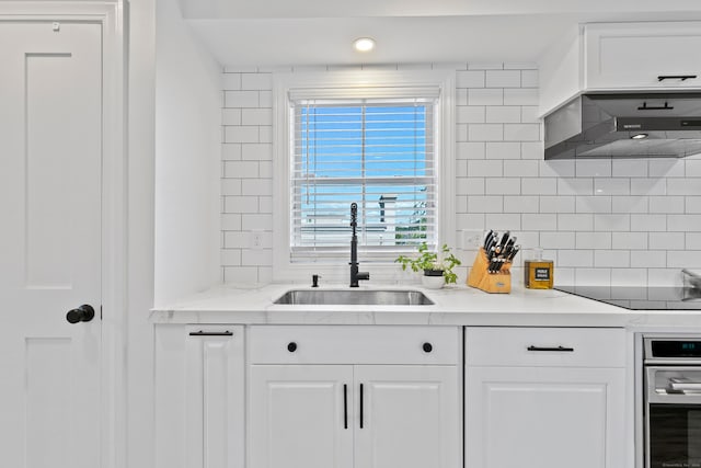 kitchen featuring black electric stovetop, sink, white cabinets, and wall chimney exhaust hood