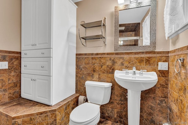 bathroom featuring a tile shower, sink, tile walls, and toilet