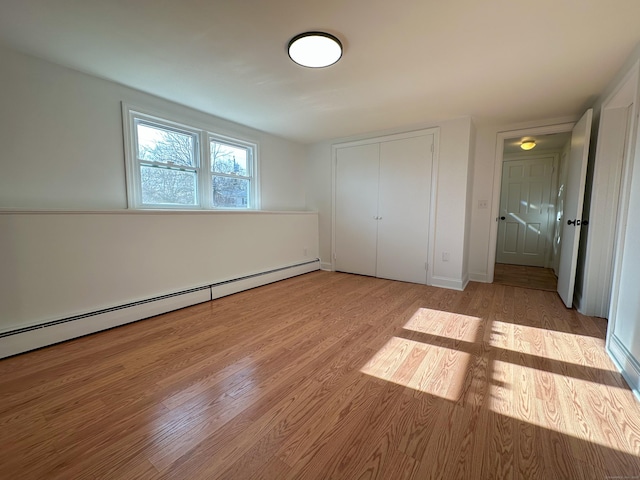 unfurnished bedroom featuring a closet, light hardwood / wood-style floors, and baseboard heating