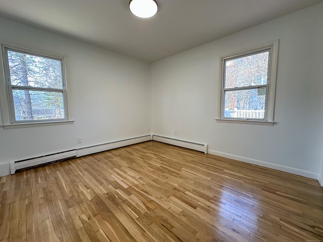 spare room featuring light hardwood / wood-style floors, baseboard heating, and a healthy amount of sunlight