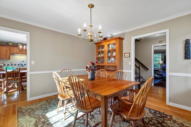 dining space with crown molding, an inviting chandelier, a textured ceiling, and light wood-type flooring