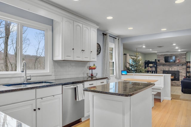 kitchen with white cabinetry, dishwasher, sink, light hardwood / wood-style floors, and a fireplace