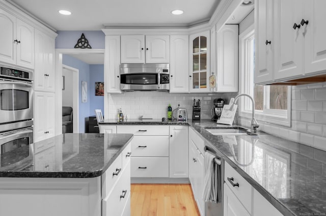 kitchen with light wood-type flooring, tasteful backsplash, stainless steel appliances, sink, and white cabinetry