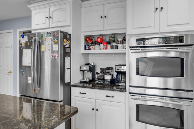 kitchen with white cabinets, decorative backsplash, stainless steel appliances, and dark stone counters