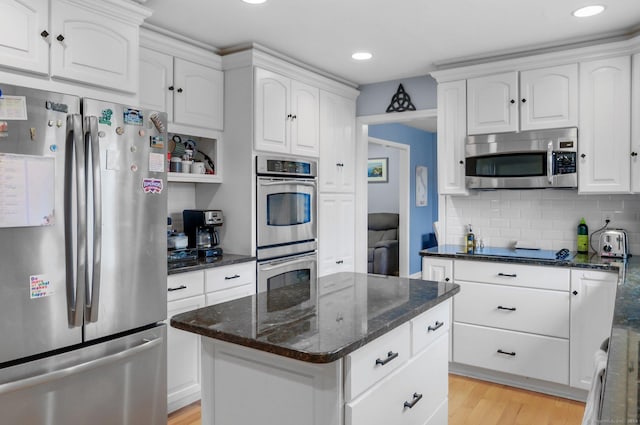 kitchen featuring white cabinetry, appliances with stainless steel finishes, dark stone counters, a kitchen island, and light wood-type flooring