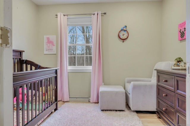 bedroom with a crib, light wood-type flooring, and a baseboard heating unit