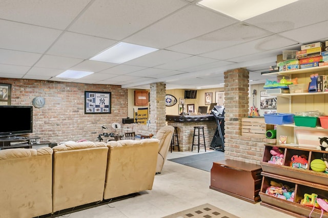 living room featuring a paneled ceiling, ornate columns, and brick wall