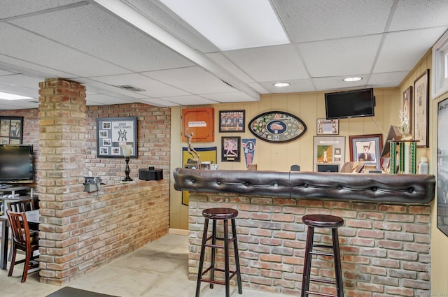 bar featuring a drop ceiling and brick wall