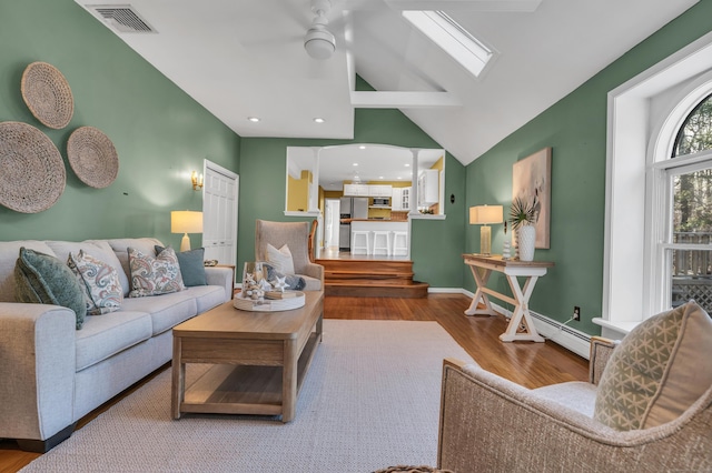 living room featuring ceiling fan, vaulted ceiling with skylight, and wood-type flooring