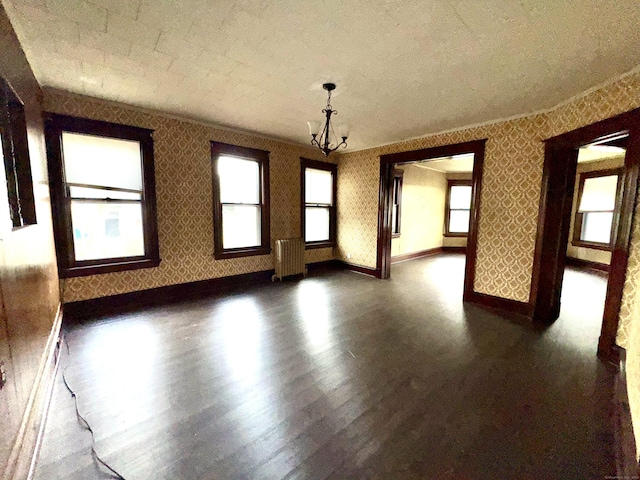 spare room featuring a chandelier, radiator heating unit, dark hardwood / wood-style flooring, and crown molding