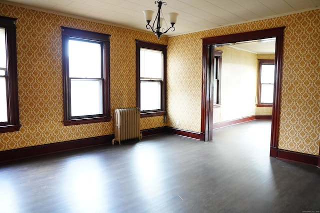 spare room with dark hardwood / wood-style floors, radiator heating unit, ornamental molding, and an inviting chandelier