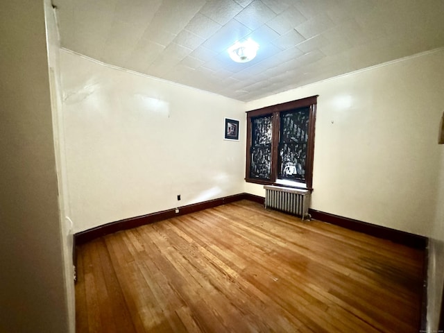 empty room with hardwood / wood-style flooring, ornamental molding, and radiator