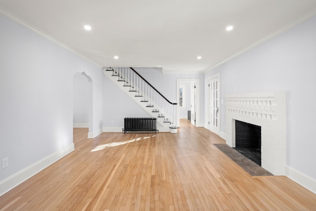 unfurnished living room with light wood-type flooring, crown molding, radiator, and a brick fireplace