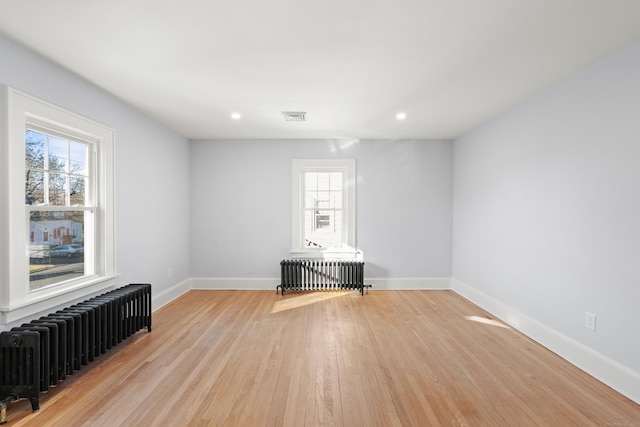 unfurnished room with radiator, a healthy amount of sunlight, and light wood-type flooring