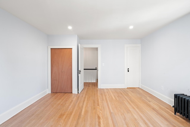 unfurnished bedroom featuring a closet, radiator heating unit, and light hardwood / wood-style flooring