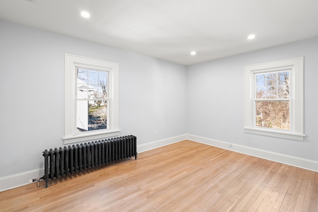 empty room with a wealth of natural light, light wood-type flooring, and radiator