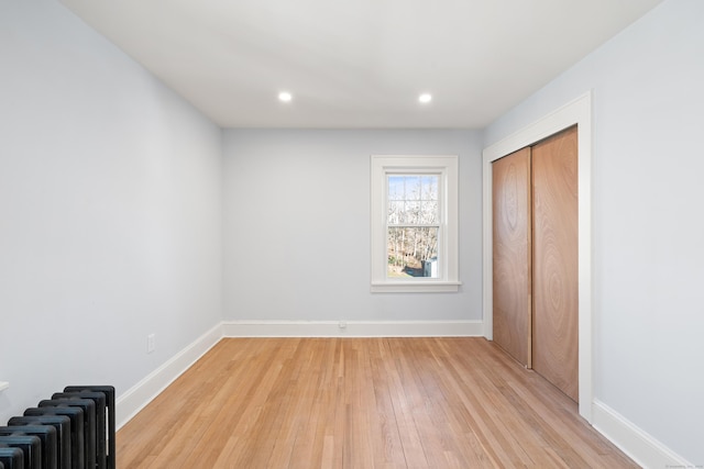 unfurnished bedroom featuring radiator heating unit, light hardwood / wood-style flooring, and a closet