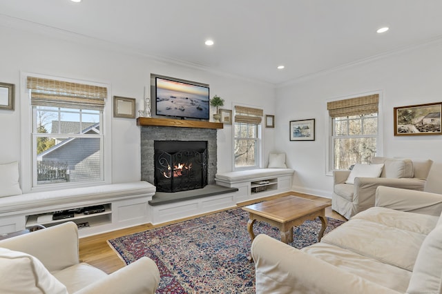 living room with light wood-type flooring, plenty of natural light, crown molding, and a stone fireplace