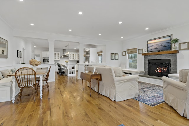 living room with light hardwood / wood-style floors, crown molding, and a stone fireplace