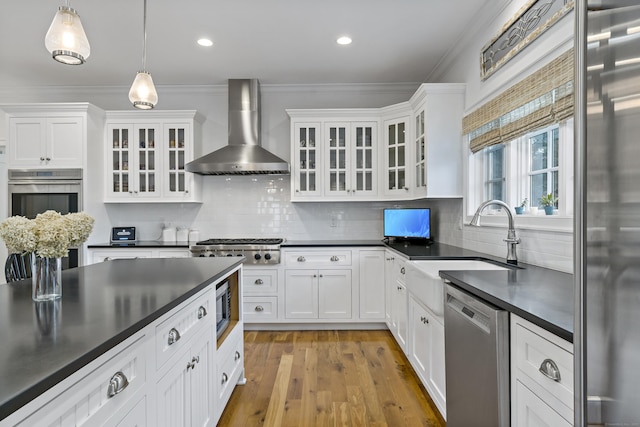 kitchen with white cabinetry, appliances with stainless steel finishes, wall chimney exhaust hood, and hanging light fixtures