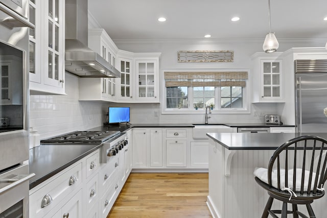 kitchen featuring white cabinets, a kitchen bar, sink, decorative light fixtures, and range hood