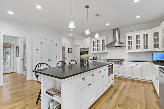 kitchen featuring decorative light fixtures, stainless steel appliances, wall chimney range hood, a breakfast bar area, and white cabinets