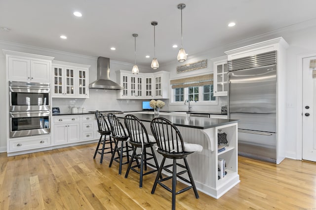 kitchen featuring stainless steel appliances, pendant lighting, wall chimney exhaust hood, white cabinets, and tasteful backsplash