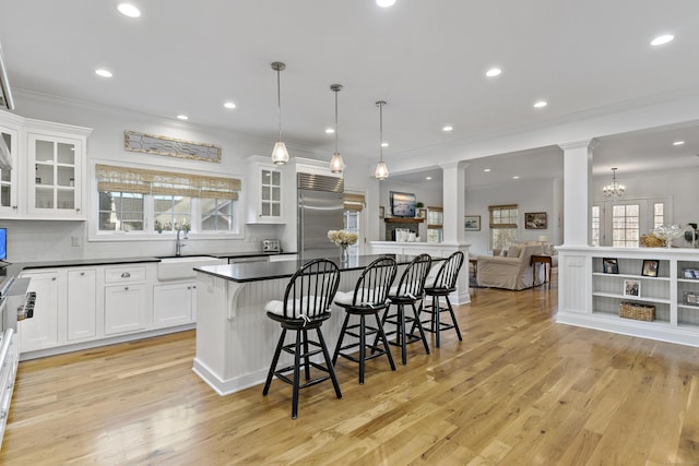 kitchen with stainless steel built in fridge, decorative light fixtures, a kitchen bar, white cabinetry, and sink