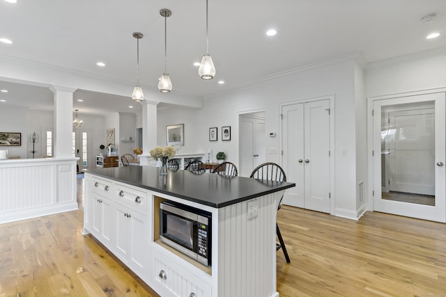 kitchen with pendant lighting, ornate columns, a kitchen island, a breakfast bar area, and white cabinets