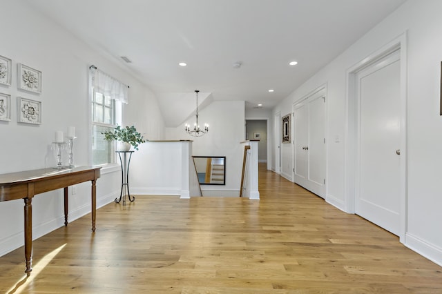 hall with lofted ceiling, light wood-type flooring, and a chandelier