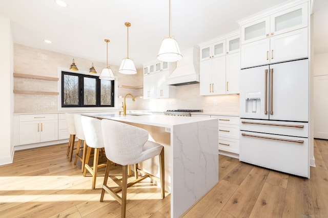 kitchen with white built in refrigerator, white cabinets, light hardwood / wood-style floors, and custom exhaust hood