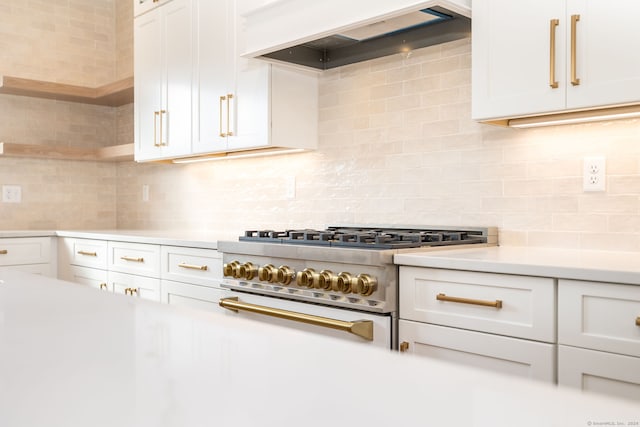 kitchen with high end stove, backsplash, white cabinetry, and custom range hood