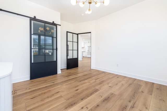 spare room with a barn door, light hardwood / wood-style floors, and a notable chandelier