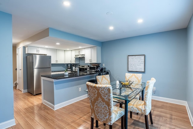 kitchen featuring white cabinets, light hardwood / wood-style flooring, dark stone countertops, appliances with stainless steel finishes, and kitchen peninsula