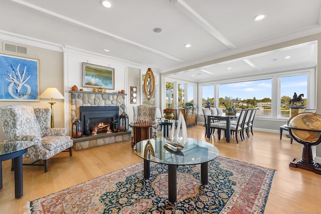 living room with beamed ceiling, crown molding, a fireplace, and light hardwood / wood-style flooring