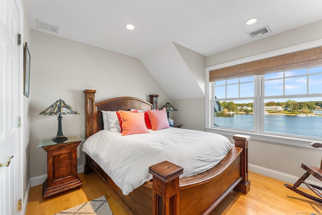 bedroom featuring light hardwood / wood-style floors, a water view, and lofted ceiling