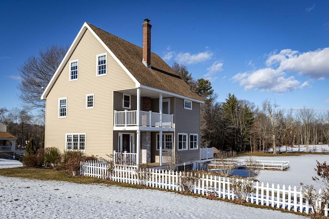 snow covered house with covered porch and a balcony