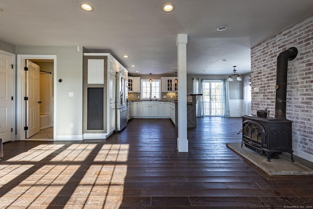 unfurnished living room with a wood stove, sink, dark hardwood / wood-style flooring, brick wall, and a notable chandelier