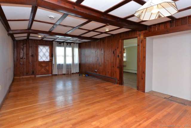 empty room featuring light wood-type flooring, coffered ceiling, a baseboard heating unit, beamed ceiling, and wood walls