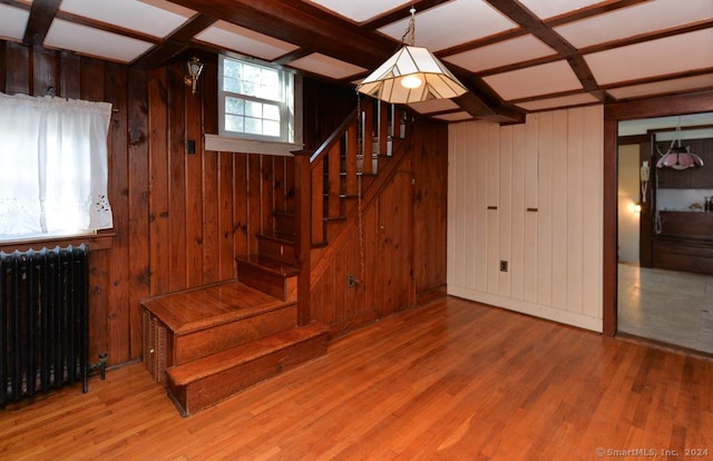 stairs featuring radiator, wooden walls, hardwood / wood-style floors, and coffered ceiling